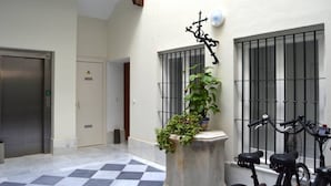 A hotel lobby with a checkered floor, an elevator, a potted plant, and a bicycle.