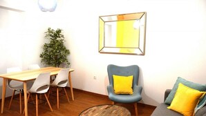 A modern living room with a wooden dining table, grey sofa, and a blue armchair with a yellow pillow.