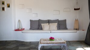 A minimalist living room with a white sofa, a small wooden coffee table with flowers, and a stone-patterned floor. - Idyllic Views one-bedroom apartment in quite and relaxing Tripiti  (Paros)