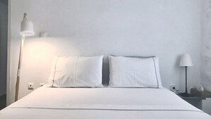 A neatly made bed with white linens, a bedside lamp, and a nightstand with a tissue box. - Idyllic Views one-bedroom apartment in quite and relaxing Tripiti  (Paros)