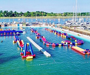 A marina with boats, inflatable water slides, and a clear blue sky. - “Rustle, Rustle Autumn’s Here” - Book Trinny’s 🍁 (Lymington)