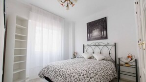 Ein Schlafzimmer mit einem Bett, einem Nachttisch, einem Wandbild und einem großen Fenster mit durchsichtigen Vorhängen.