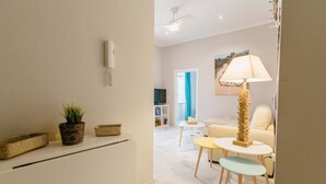 Een moderne woonkamer met een bank, een salontafel en een lamp. Er staat een plant op een plank en een telefoon hangt aan de muur.