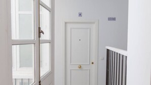Een witte deur met een messing deurklink, een klein bordje erboven en een metalen hekwerk aan de rechterkant.