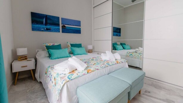 Een slaapkamer met een grote spiegel, twee bedden met identiek smaragdgroen beddengoed, en kunst aan de muur.