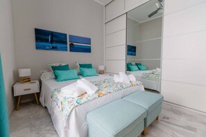 A bedroom with a large mirror, two beds with matching teal bedding, and artwork on the wall.