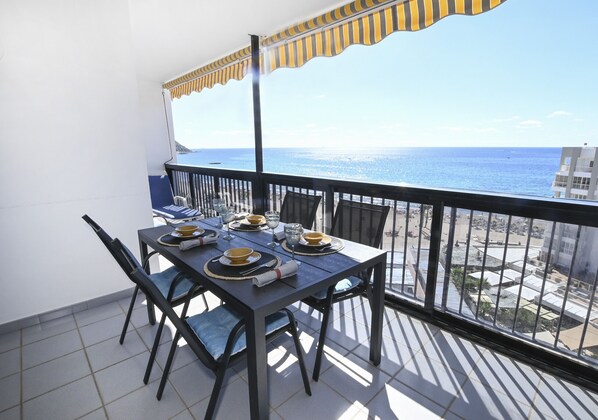A balcony with a table set for dining, overlooking a coastal view.