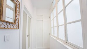 Un couloir étroit aux murs blancs, une porte en bois et une grande fenêtre à vitres dépolies.
