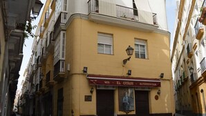 Un bâtiment jaune avec une porte fermée, une enseigne indiquant « BAR - EL CHOR - ULTRAMAR » et une affiche représentant un homme.