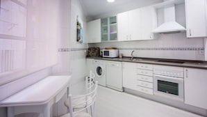Une cuisine compacte avec des meubles blancs, un four à micro-ondes, un lave-linge et un évier.