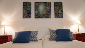 Un lit double agrémenté d’oreillers à motifs, deux tables de chevet avec des lampes et trois tableaux abstraits accrochés au mur.