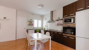 Una cocina moderna con armarios de madera, encimera blanca y comedor con mesa y sillas blancas.