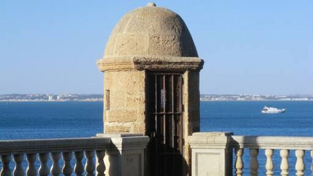 Una estructura de piedra con una cúpula y una puerta, con vista a una masa de agua y una costa distante.