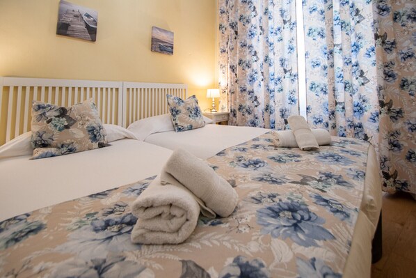 Een hotelkamer met twee bedden, bloemenbeddels, een hoofdbord, een nachtkastje met een lamp en gordijnen met een bloemenprint.