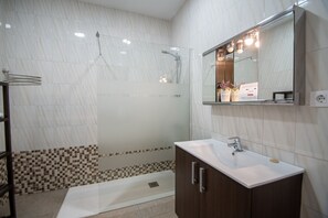 Un baño moderno con ducha acristalada, lavabo blanco y tocador de madera.