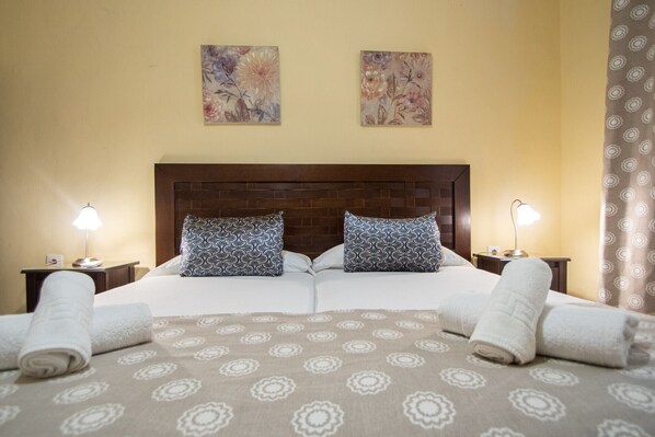 Una cama doble con una colcha estampada, dos almohadas a juego, dos lámparas de noche y dos cuadros en la pared.