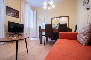 Una sala de estar con televisor, sofá, mesa de comedor con sillas y candelabro.