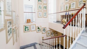 A staircase with white balusters and a wooden handrail, surrounded by framed botanical illustrations on the walls. - Duplex de la Botanica - Cadiz (Cádiz)