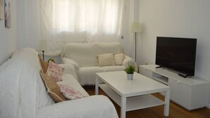Un saló amb un sofà blanc, una taula de centre blanca, un televisor de pantalla plana i una làmpada.