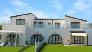 Une maison moderne à deux étages, dotée d’un balcon, de grandes fenêtres et d’une pelouse bien entretenue.