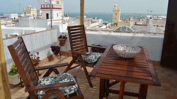 A wooden table and two chairs on a rooftop terrace with a view of the city and sea. - El Mirador de Cádiz (C��diz)