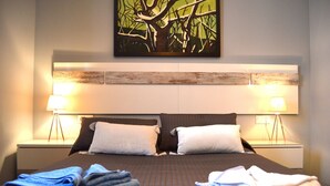 A neatly made bed with folded towels, two bedside lamps, and a painting above the headboard. - El Mirador de Cádiz (C��diz)