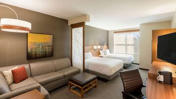 A hotel room with a sofa, two beds, a desk, a coffee maker, and a TV.