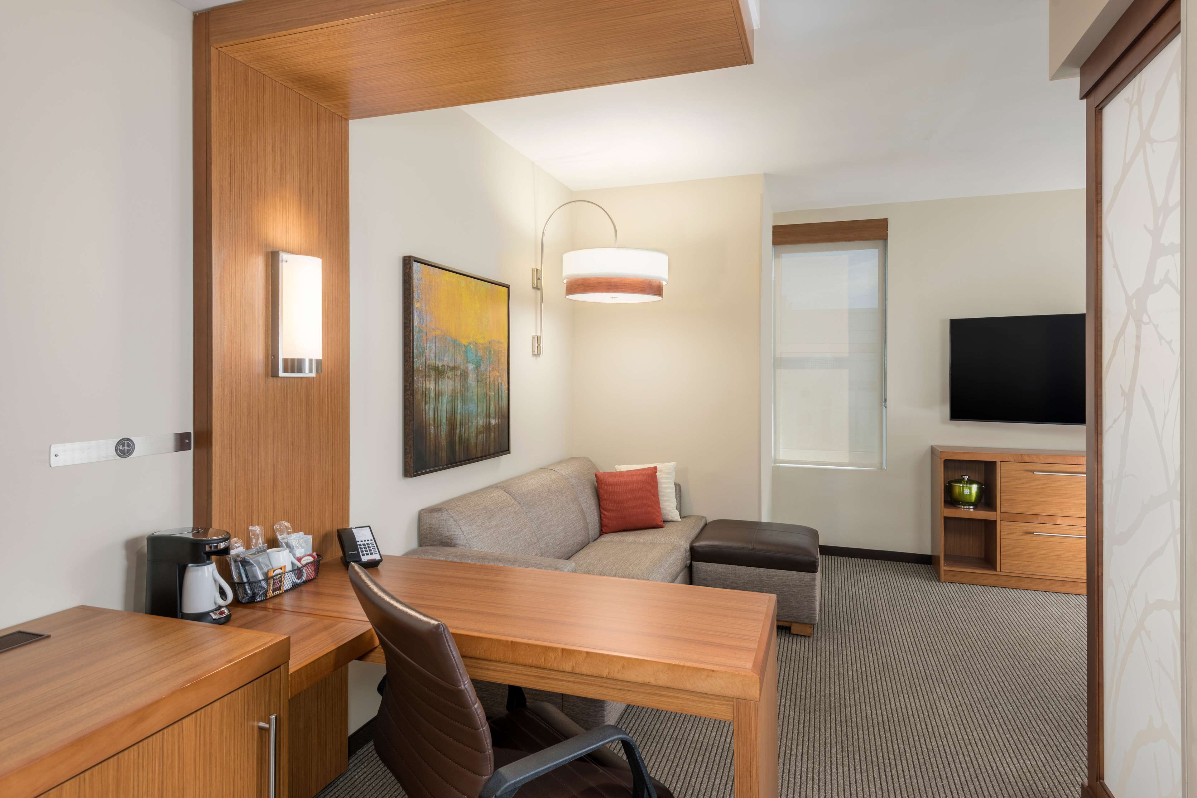 A hotel room with a wooden desk, a sofa, a television, and a painting on the wall.