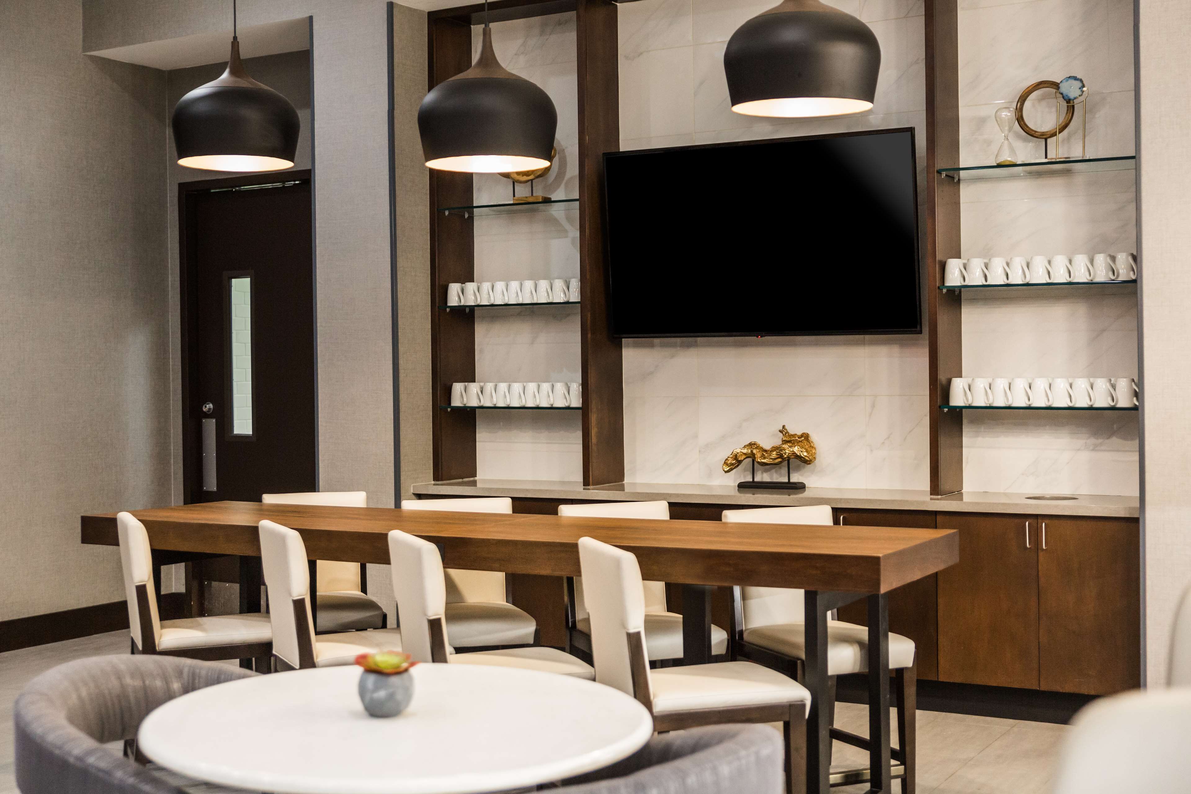 Un espace repas moderne avec une table et des chaises en bois, une table ronde agrémentée d’un vase, des luminaires suspendus, un téléviseur à écran plat et un pare-feu en marbre.