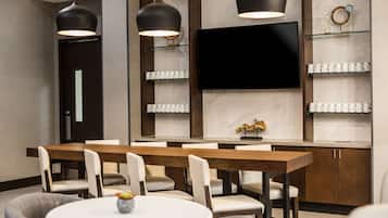 A modern dining area with a wooden table and chairs, a round table with a vase, pendant lights, a flat-screen TV, and a marble backsplash.