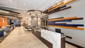 Een moderne hotel lobby met een receptiebalie, een zithoek en een decoratieve wand.
