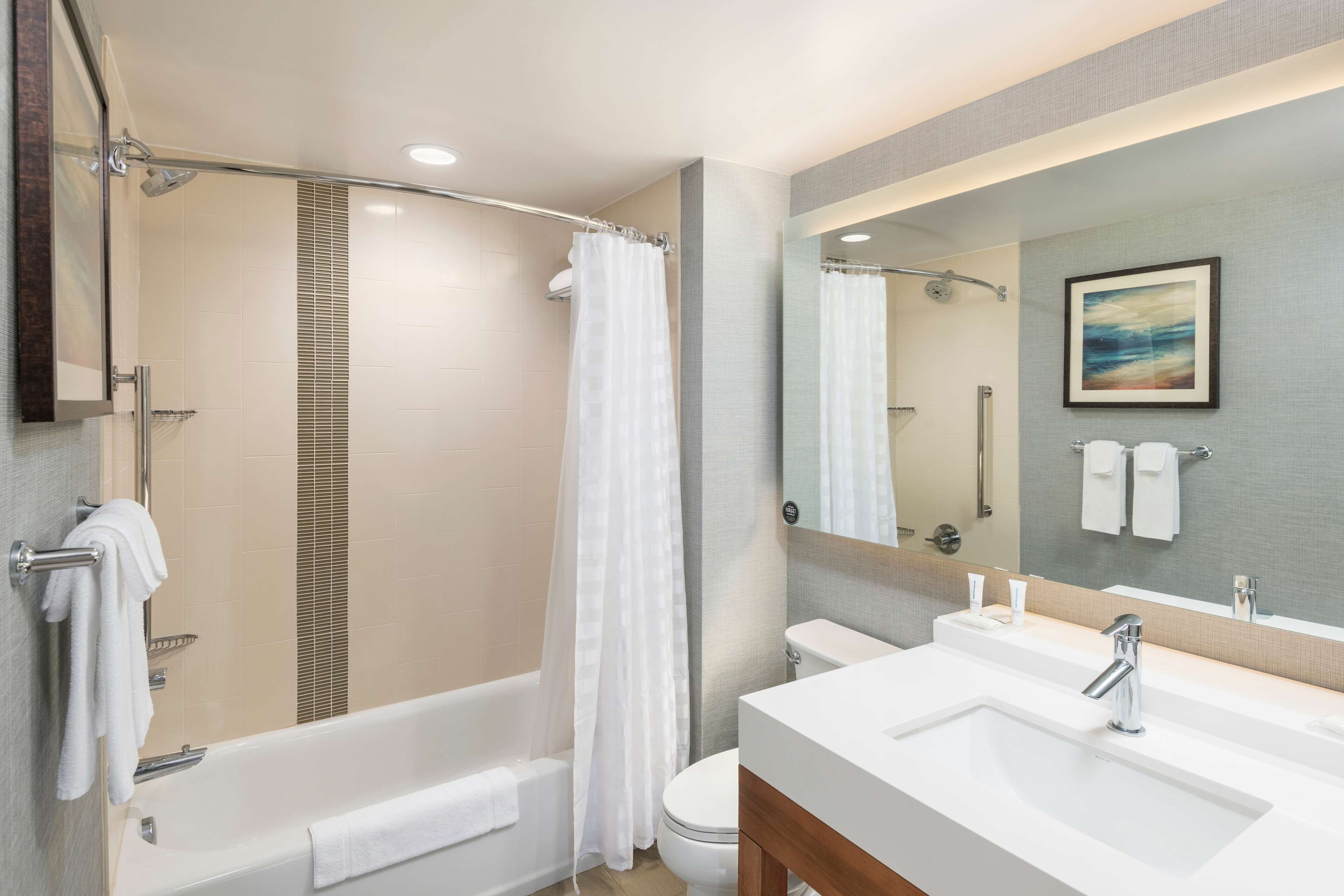 Een moderne badkamer met een bad, douche, toilet en wastafel met een grote spiegel.