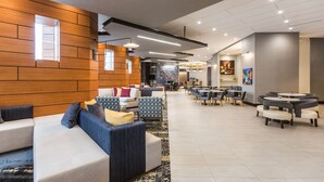 Een moderne hotellobby met diverse zithoeken, waaronder banken en tafels, en een kamerbreed tapijt met een patroon.