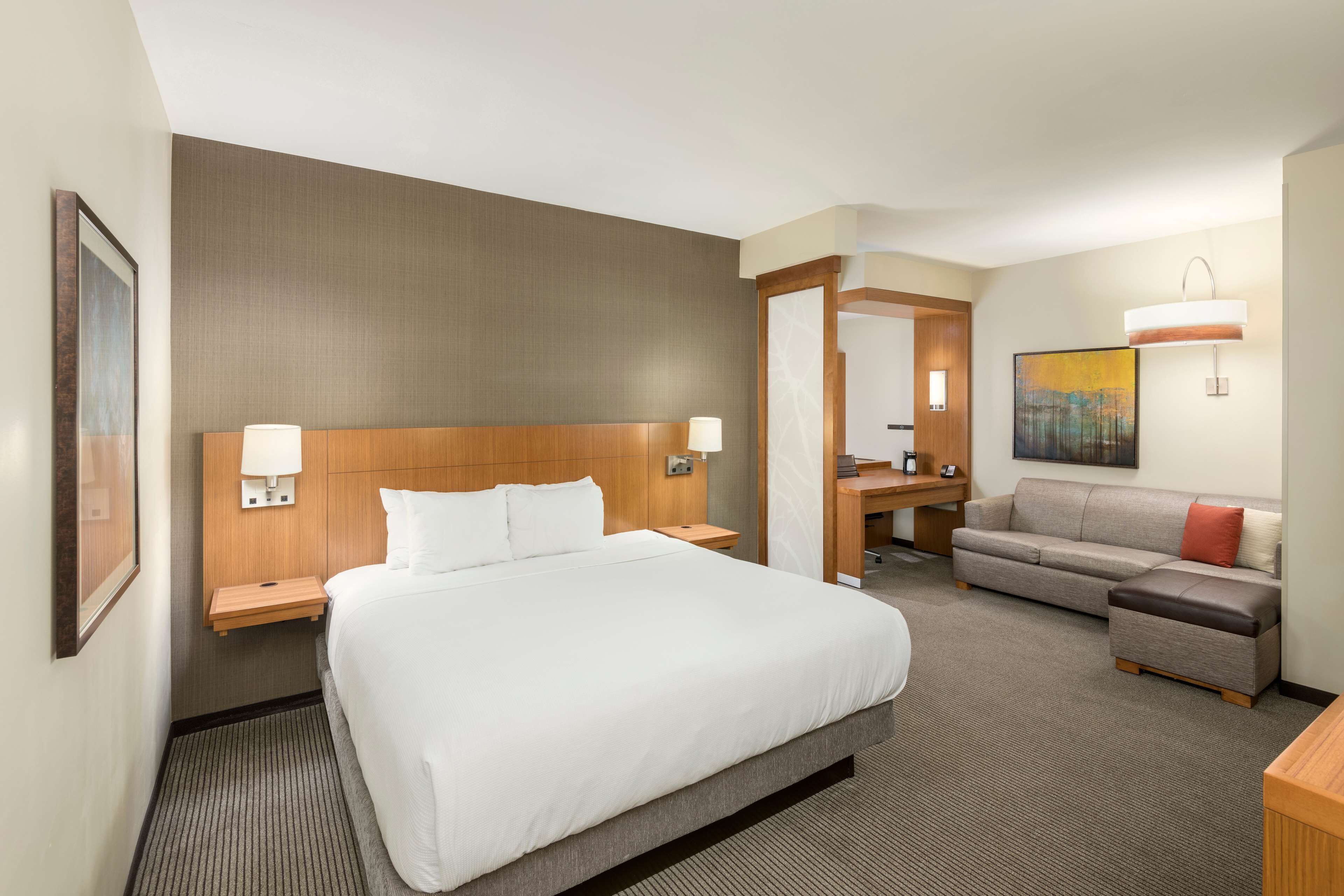 A hotel room with a large bed, a sofa, a desk, and a mirror.
