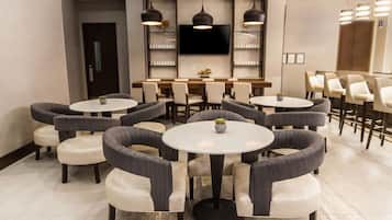 A hotel lobby with round tables and chairs, a TV mounted on the wall, and a reception desk.