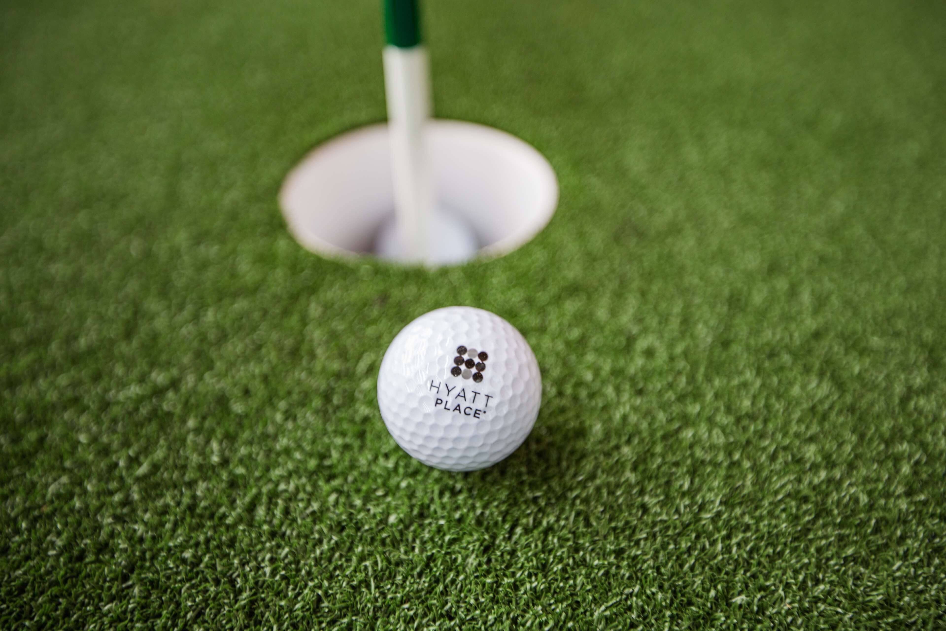 En golfboll på konstgräs, med ett hål synligt i bakgrunden.