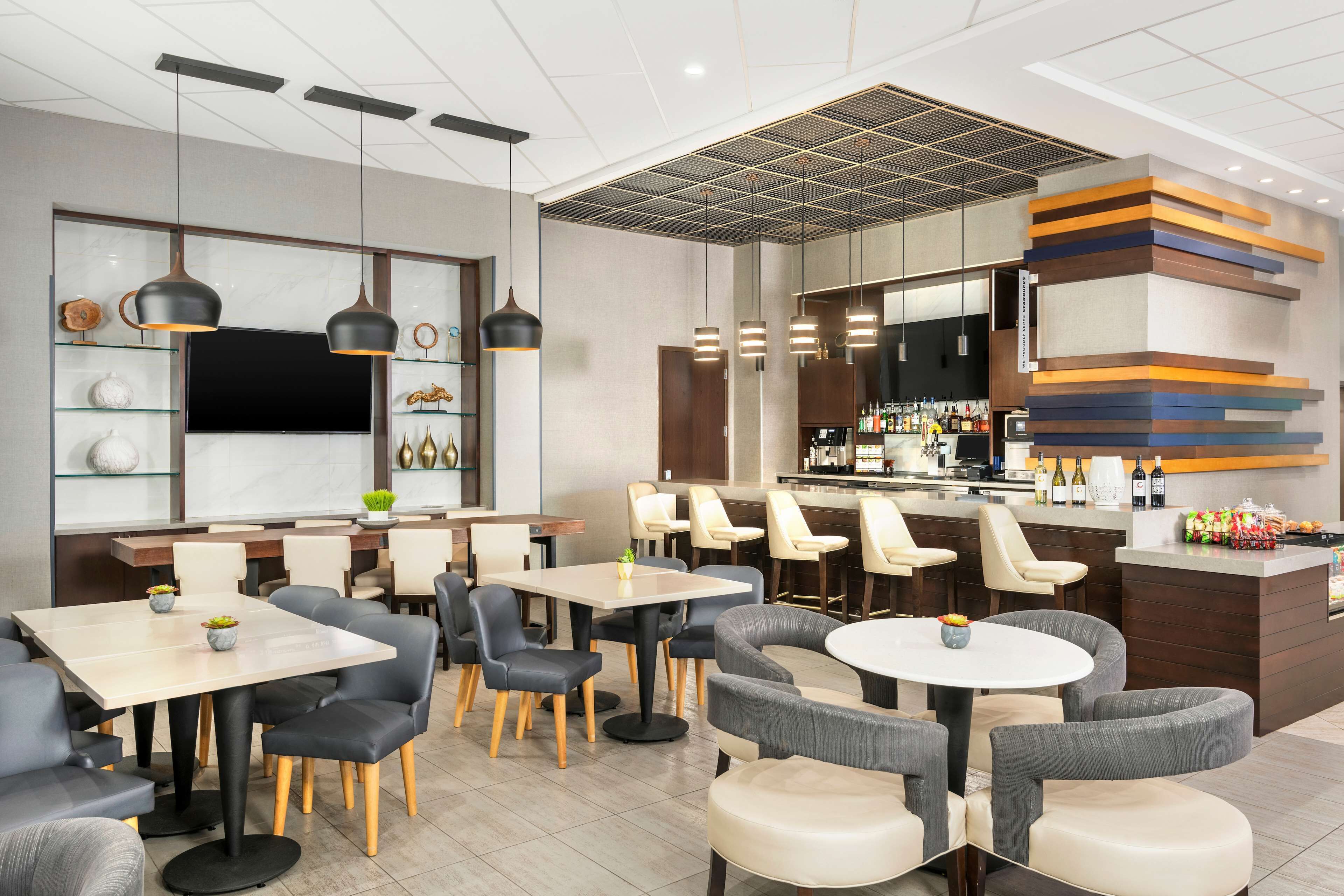 A modern restaurant with multiple seating areas, including round and square tables, and a bar counter with a variety of beverages.