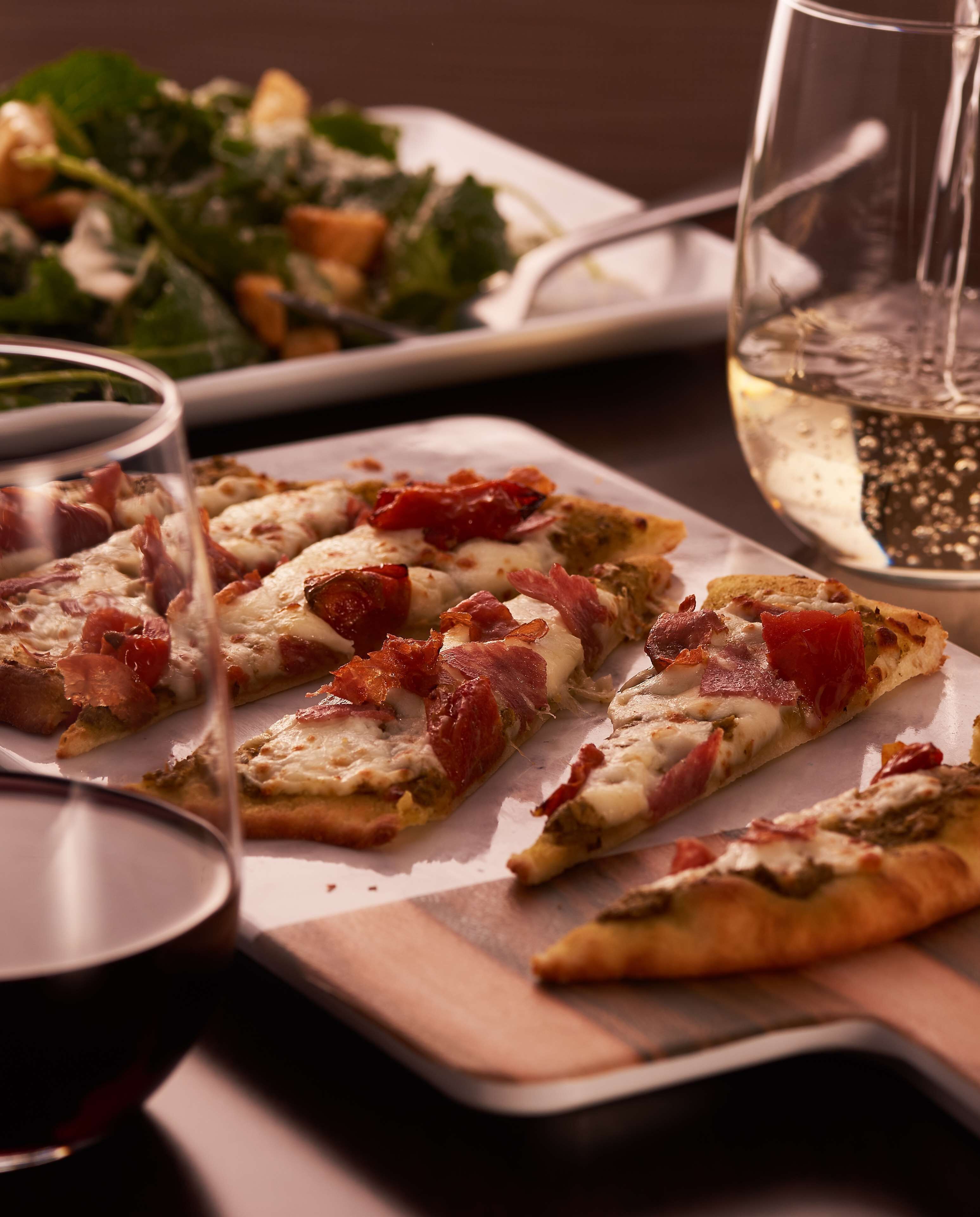 Une table à manger avec une pizza, un verre de vin blanc et une salade.