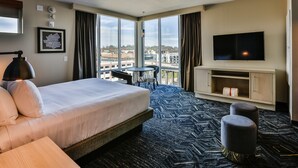 Hotelkamer met een groot bed, een televisie, een bureau en uitzicht op de stad door grote ramen.