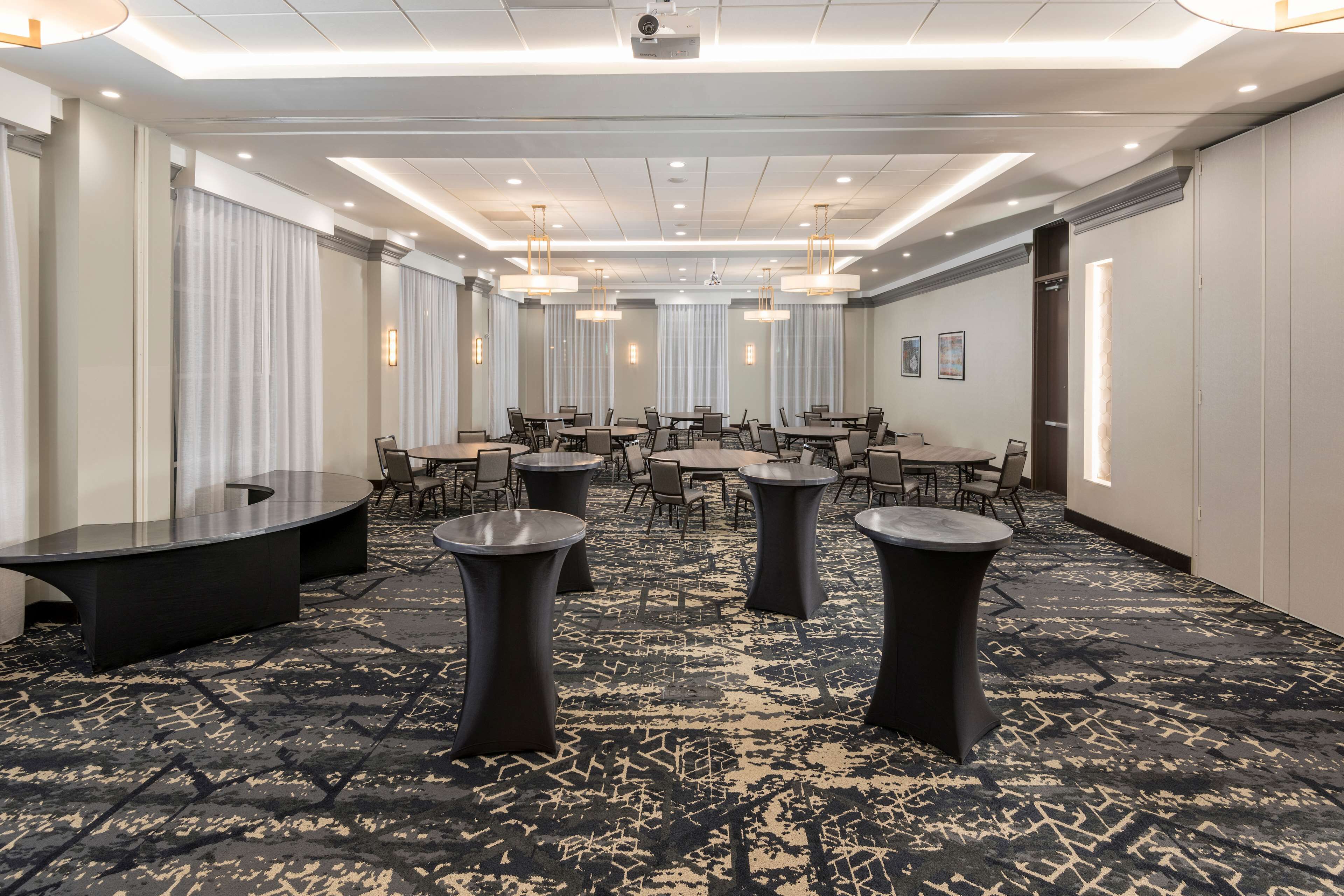 A spacious conference room with multiple tables and chairs, a patterned carpet, and recessed lighting.