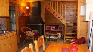 Ein gemütliches Blockhaus-Interieur mit einem Holzespeisetisch, Korbstühlen, einem Kamin und einer Treppe mit Herzdekorationen.