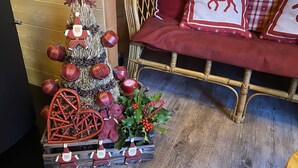 Ein gemütliches Zimmer mit Holzboden, einer Rattan-Couch mit roten Kissen und einem kleinen Weihnachtsbaum mit Dekorationen und einem Stern auf der Spitze.