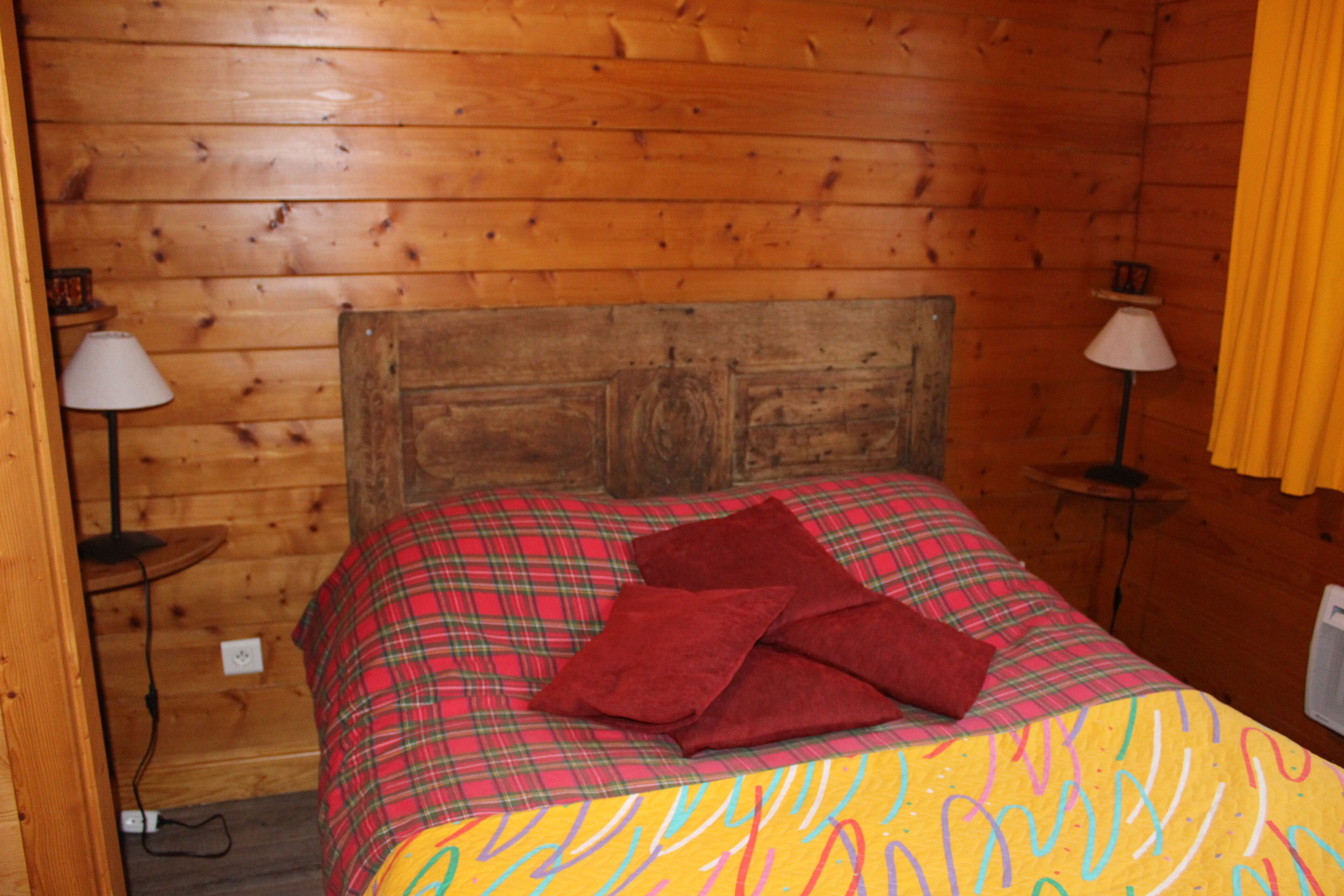 L’intérieur d’un chalet en bois comprend un lit, deux tables de chevet et une fenêtre avec des rideaux.