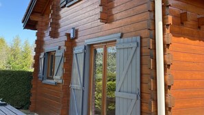 Eine Holzhütte mit zwei Fenstern und einer Tür, ein Picknicktisch davor und ein klarer Himmel.