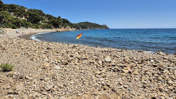 A rocky beach with a flag, clear blue sky, and distant buildings. - 2 rooms with Big terrace of 25m ² in 350M of the Beach (ST MANDRIER SUR MER)