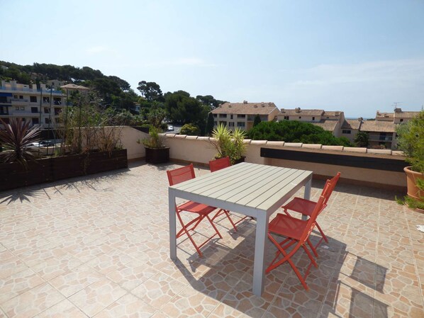 An outdoor patio with a table and chairs, surrounded by potted plants and a view of buildings in the background. - 2 rooms with Big terrace of 25m ² in 350M of the Beach (ST MANDRIER SUR MER)