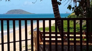 A beach view through a wooden fence with palm trees and a distant island. - Escape with the sound of the waves (Deshaies)