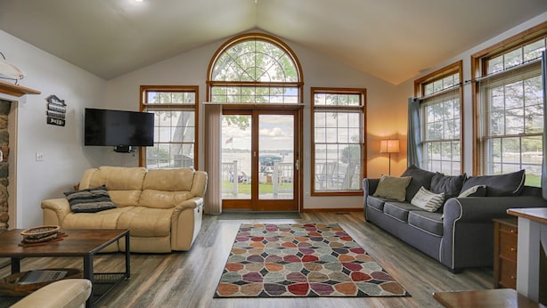 A spacious living room with a large window, a fireplace, and a television. - Riesling Rod and Reel: Fishers Paradise (Honeoye)