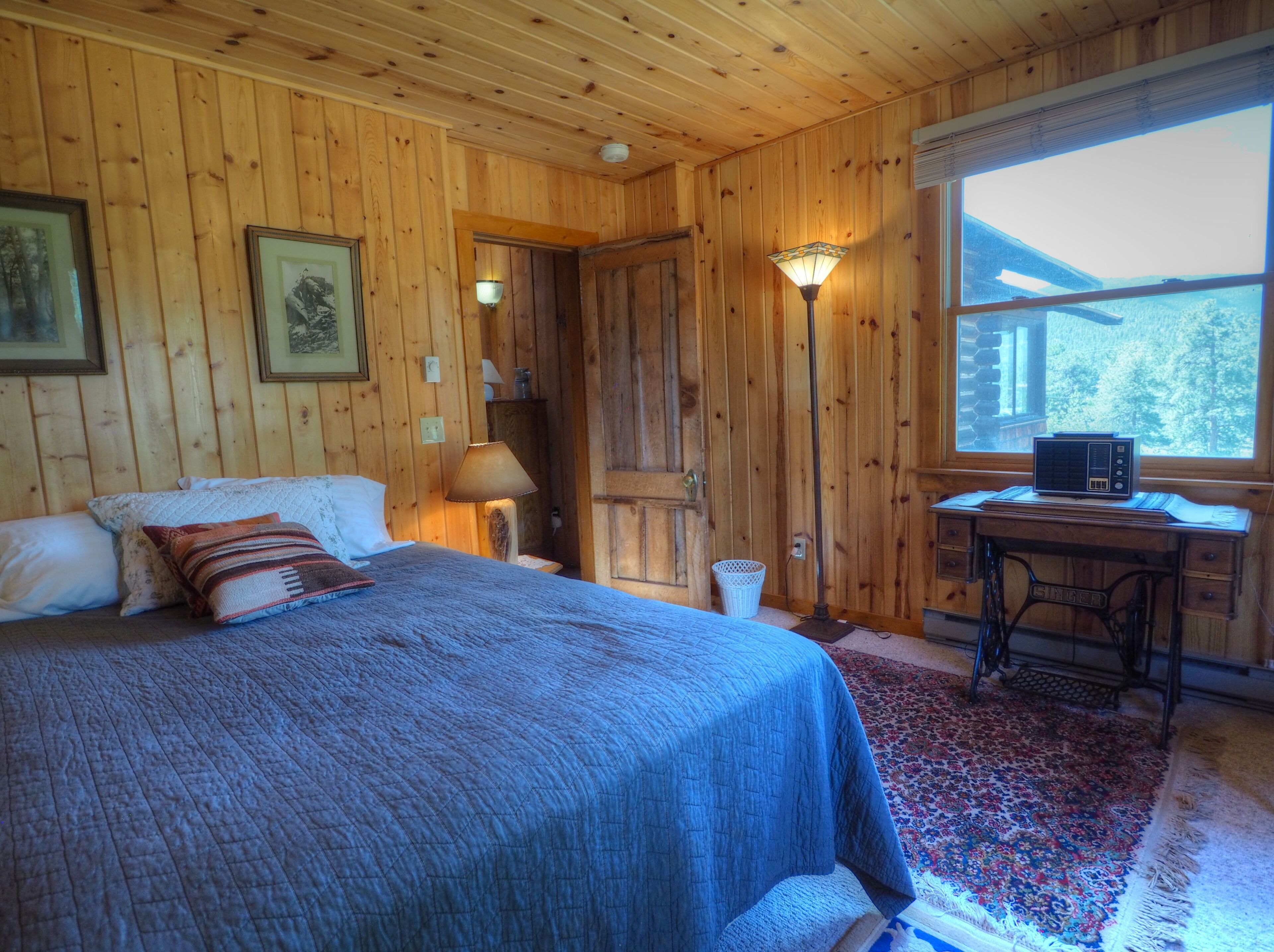 A wooden-paneled room with a bed, a desk, a lamp, and a radio.