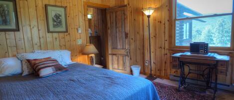 A wooden-paneled room with a bed, a desk, a lamp, and a radio.
